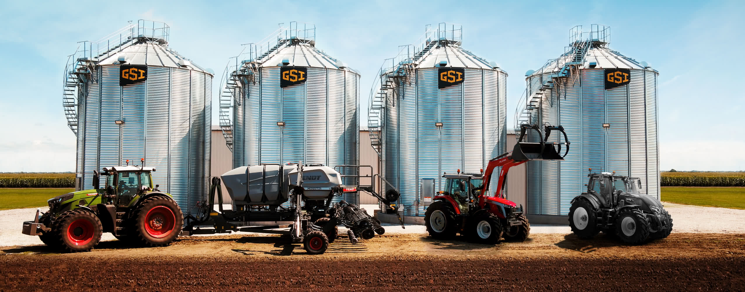 Three tractors, of differing models, are parked in front of four GSI branded grain silos